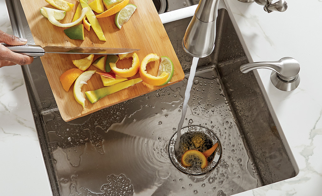 A person placing citrus peels down a garbage disposal