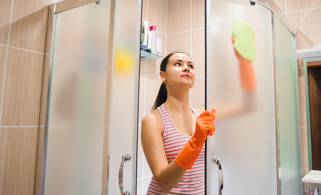 A person cleans a glass shower door with a sponge