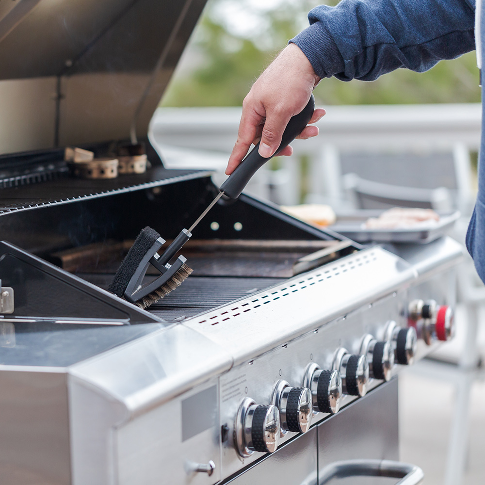 A man cleaning an open grill with a brush.