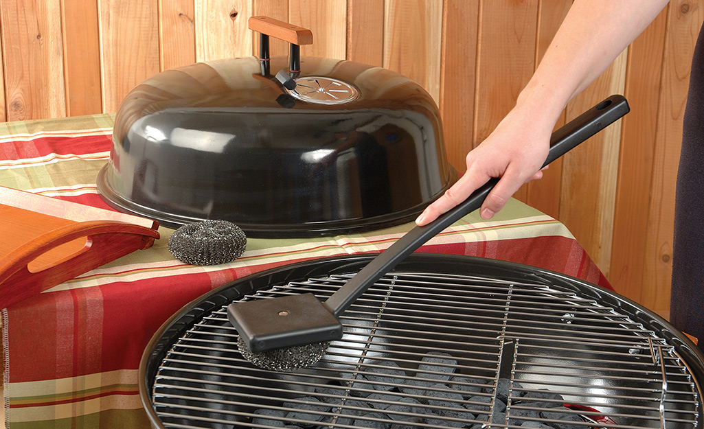 Someone cleaning a charcoal grill.