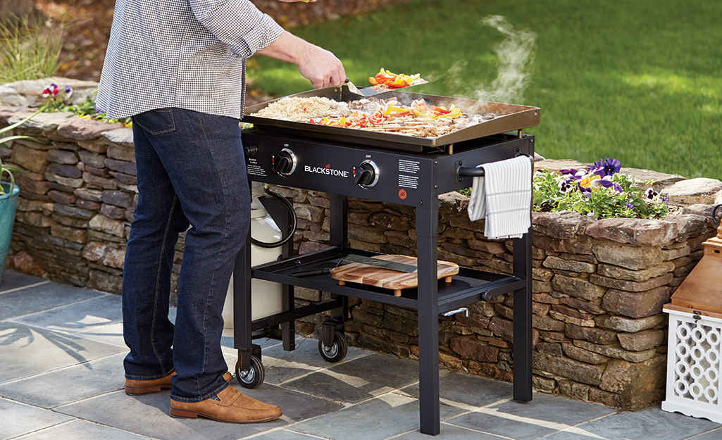 Someone cooking outside on a flat top grill.