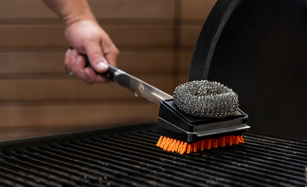 Someone using a two-sided grill cleaning tool.