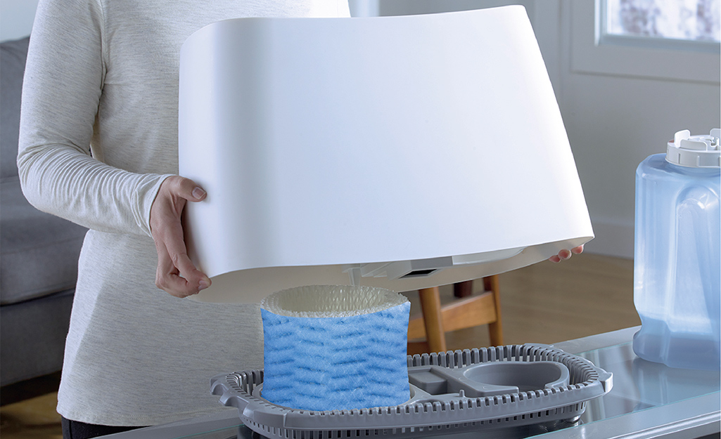 A person lifting the top off a humidifier to reveal the air filter.