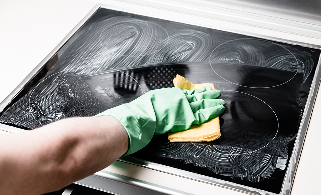 A person cleaning an electric stovetop with a cloth.