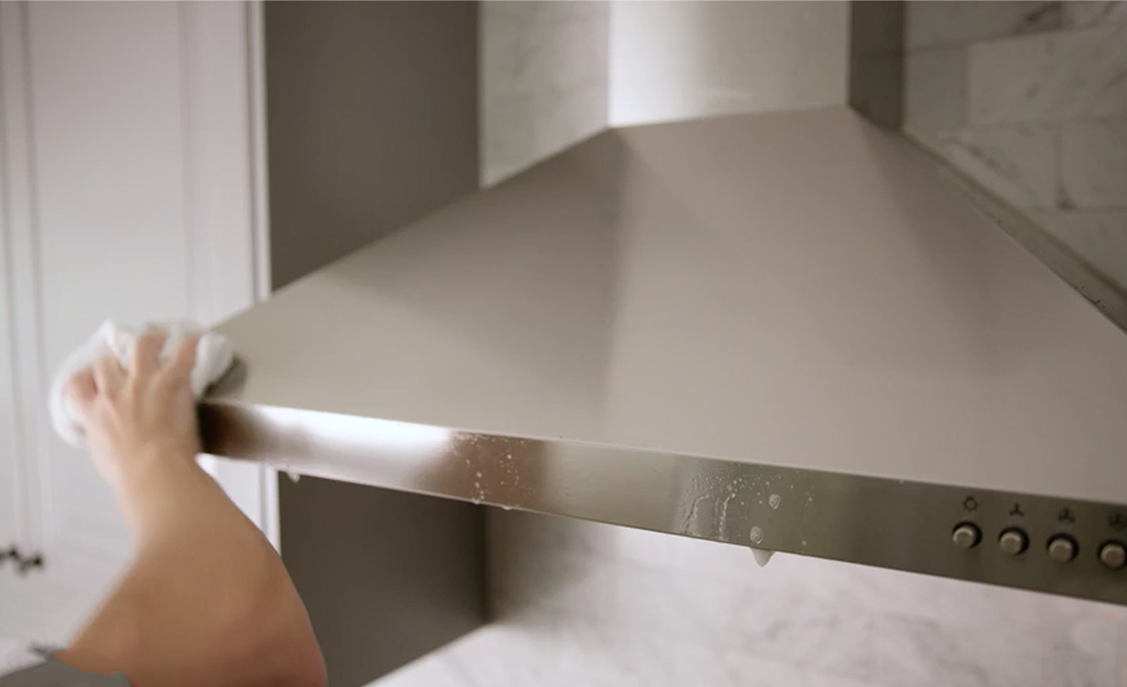 A person cleaning a range hood with a cloth.