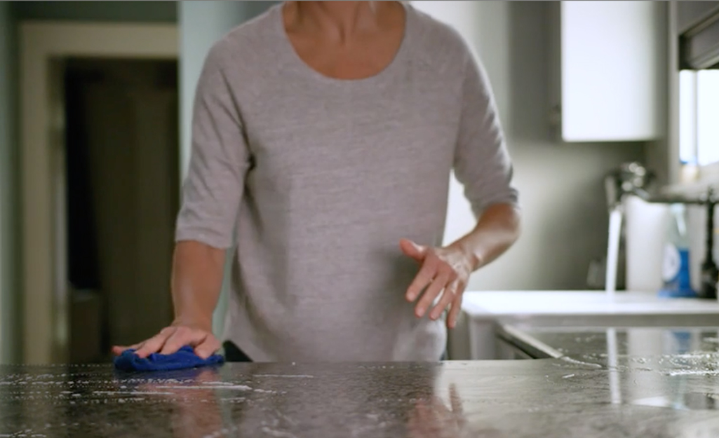 A person wiping down kitchen countertops with a cloth.