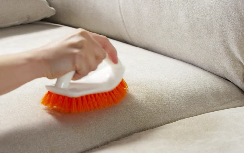 A person brushes the seating of a microfiber couch after it has dried.
