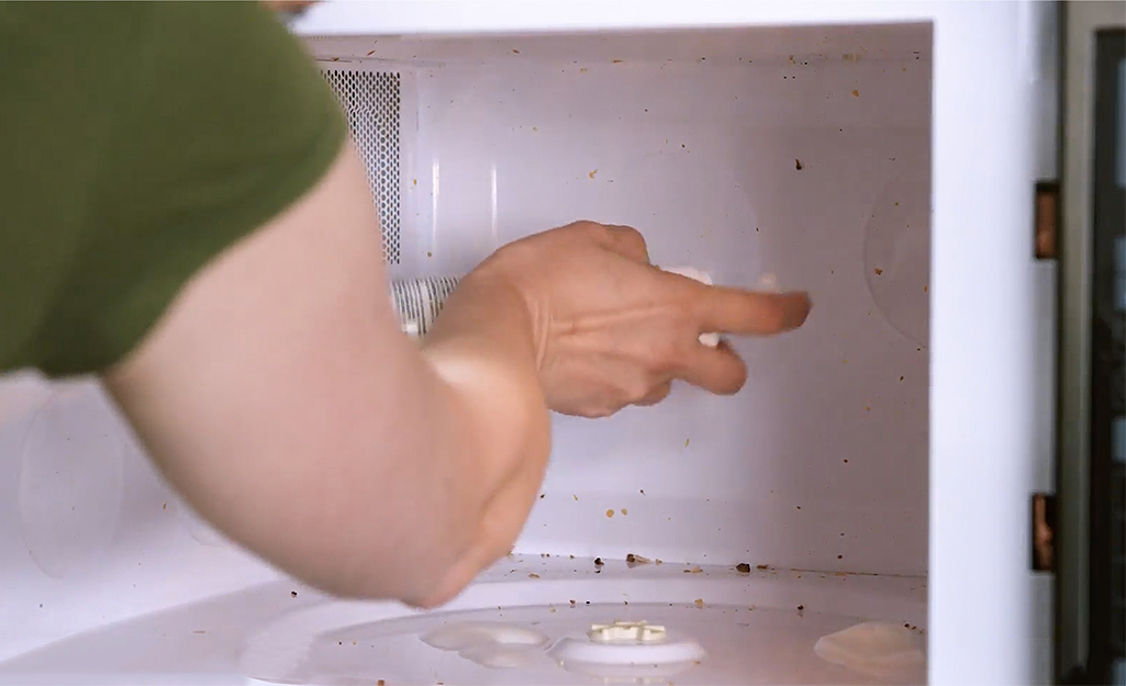 A woman sprays cleanser on the interior surfaces of a soiled microwave.