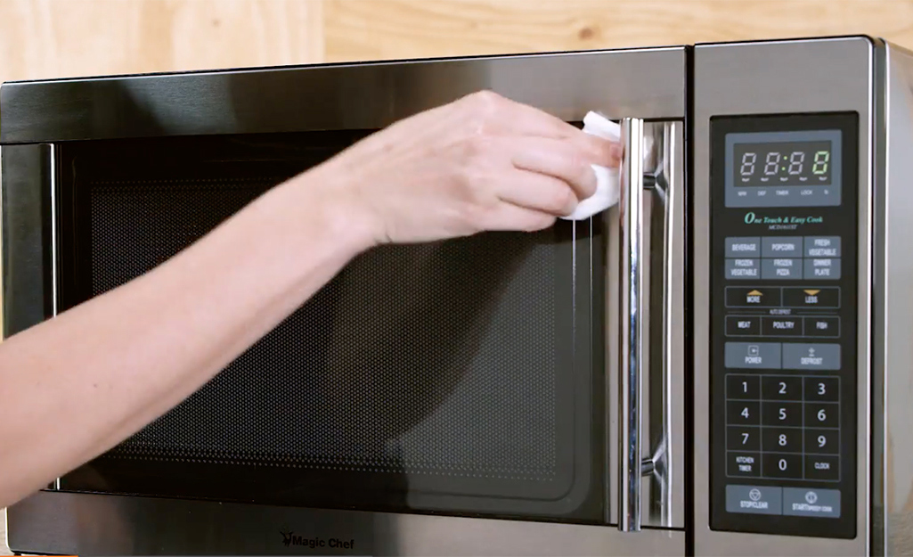 Woman wipes down the front door of a microwave with a paper towel.