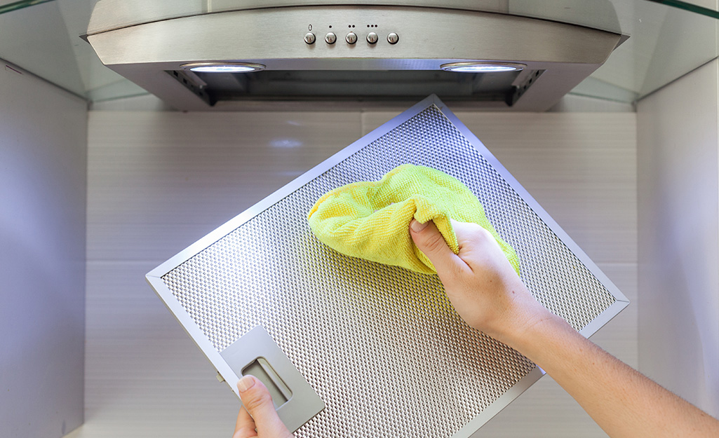 A person wipes the filter of a cooking range hood with a cloth.