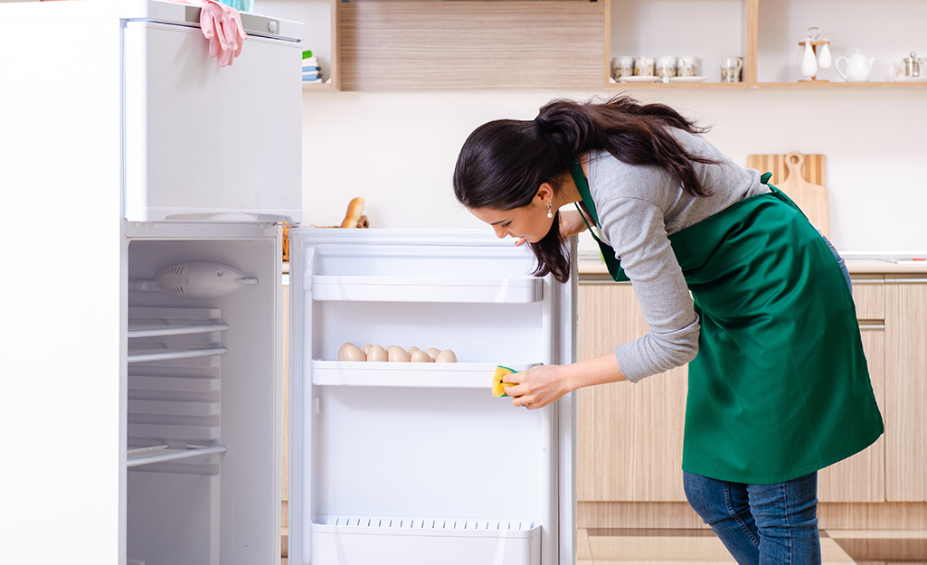 A person uses a sponge to wipe the interior door of a refrigerator.