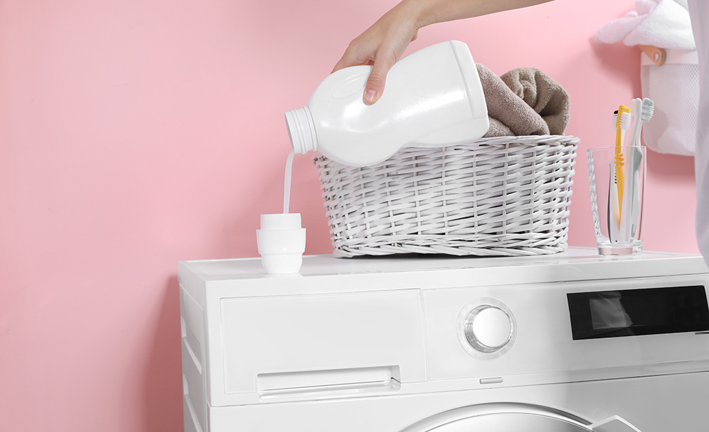 A person pours laundry cleaner into a cap atop a white washing machine.