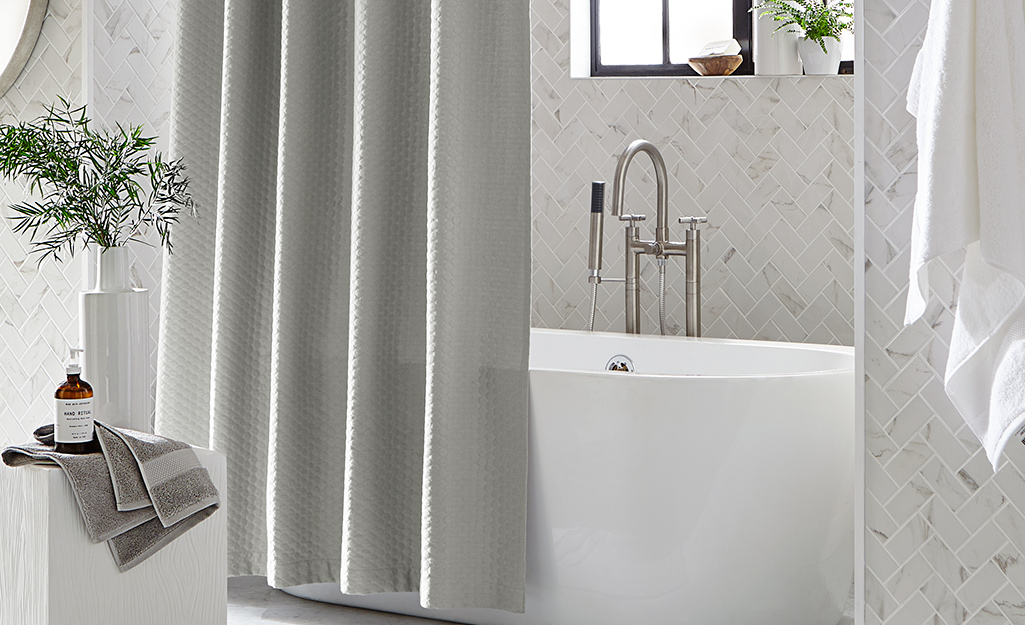 A gray shower curtain hangs outside a bathtub in a white bathroom.