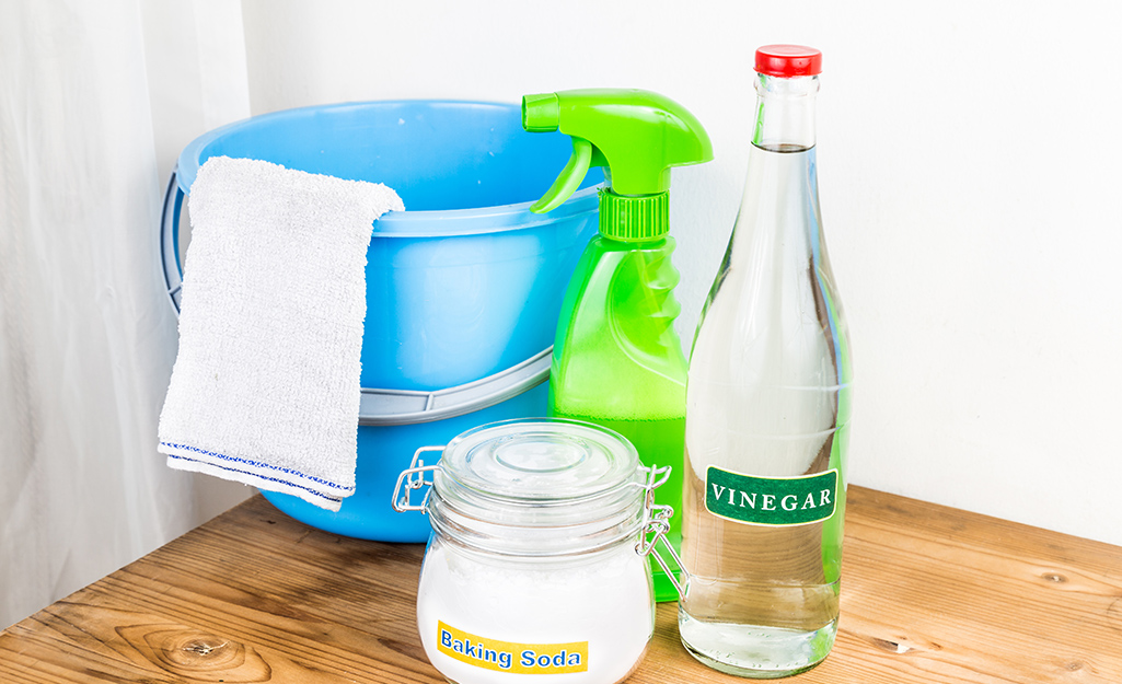 Vinegar, baking soda and a spray bottle stand next to a bucket for mixing a cleaning solution.