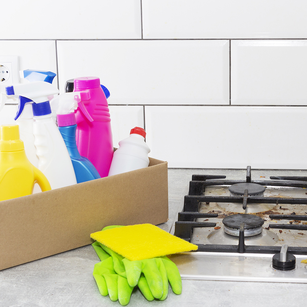 Brightly colored cleaning products sit in a box beside a gas stove top.