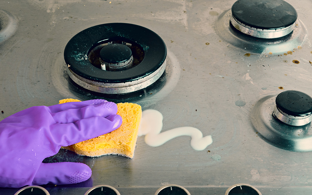 A person cleans with a sponge around burners on a stove top.