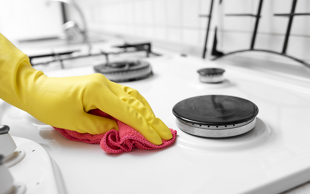 Someone wearing yellow gloves uses a cloth to clean a gas stove top.