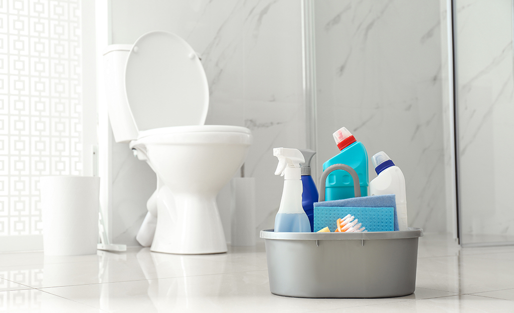 A gray container filled with toilet cleaning supplies sits in a white bathroom.