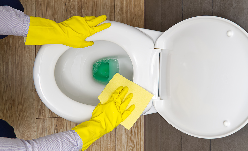 Someone wearing yellow gloves cleaning toilet.