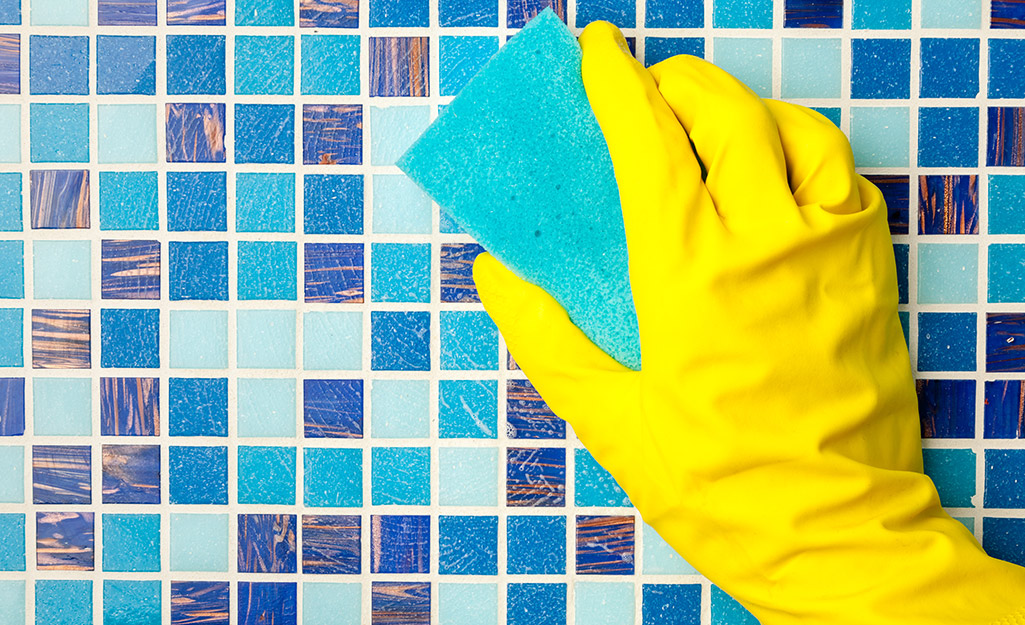 A gloved hand cleaning a wall of tile.