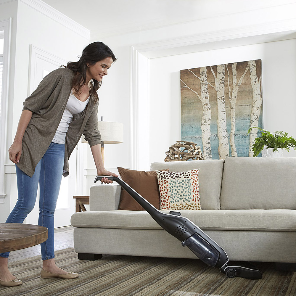 A woman uses a vacuum cleaner on a living room rug.