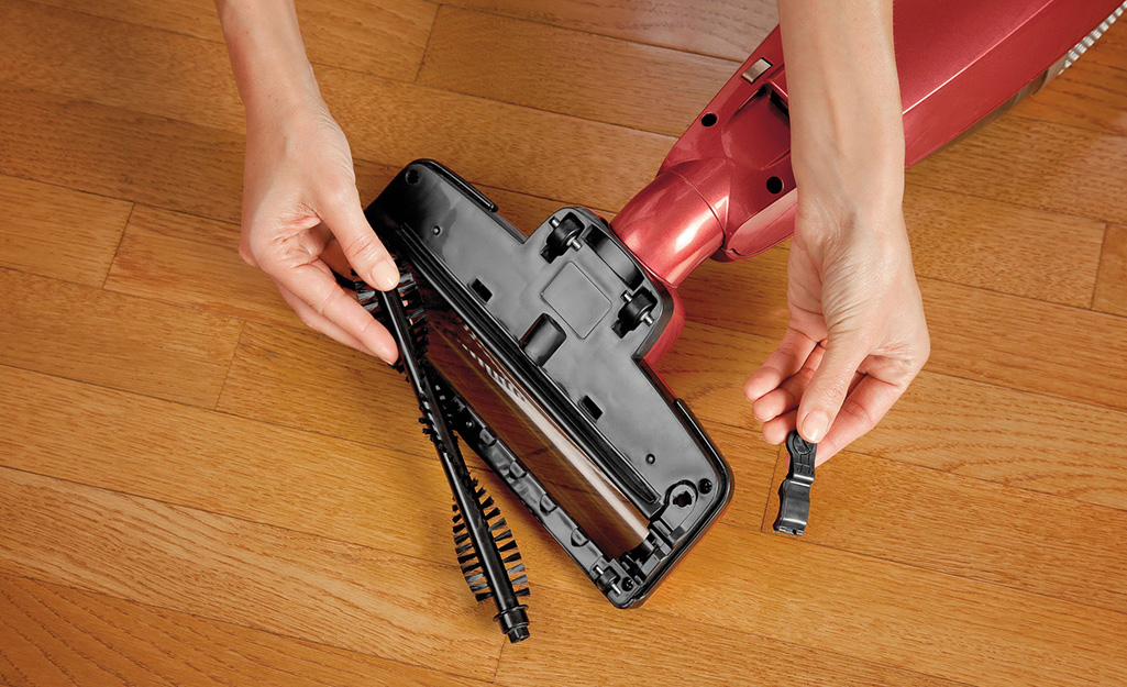A person removes a roller brush head from a vacuum cleaner.