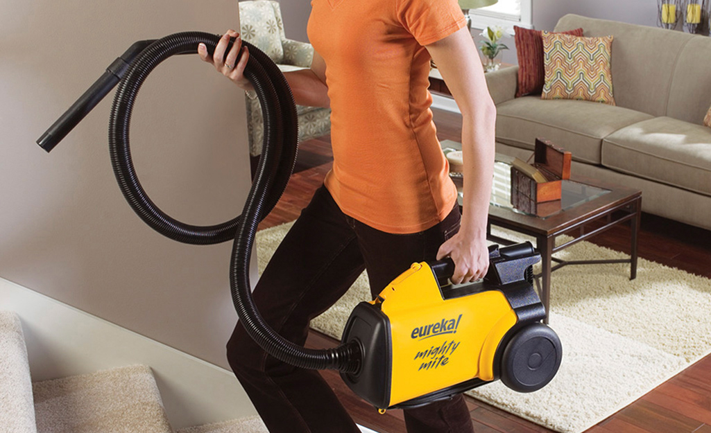 A person walks upstairs while holding a vacuum cleaner and hose.