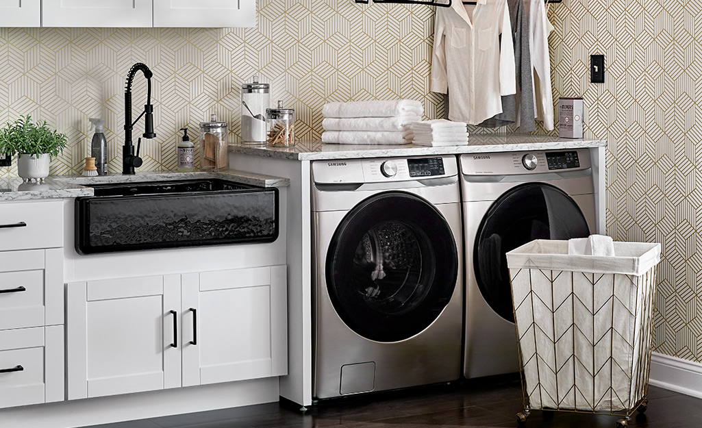 A kitchen with a front-load washer, dryer and hamper in the corner.