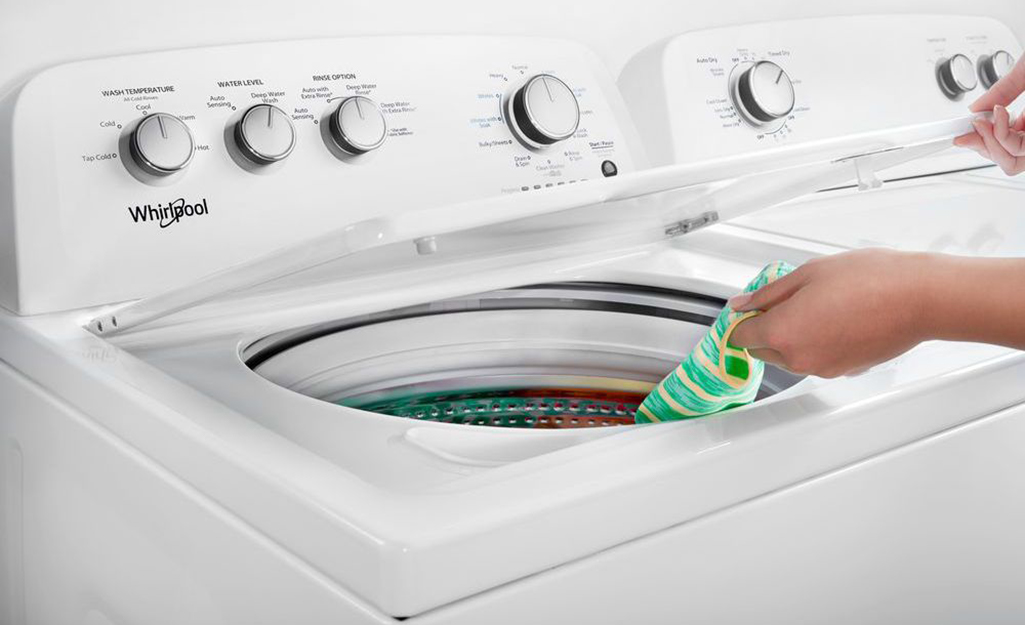Someone places a sock in a clean top-load washing machine.