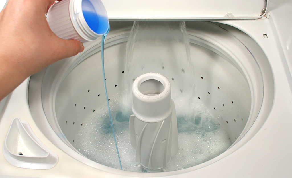 Someone pouring oxygen bleach into a top-load washer tub full of washing soda.