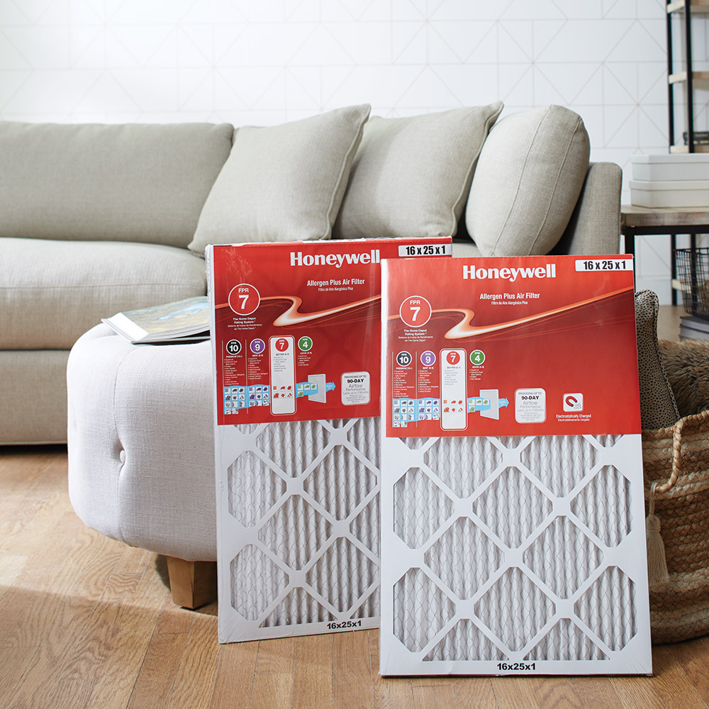 Two new air conditioner filters stand upright on the floor, leaning against a couch.