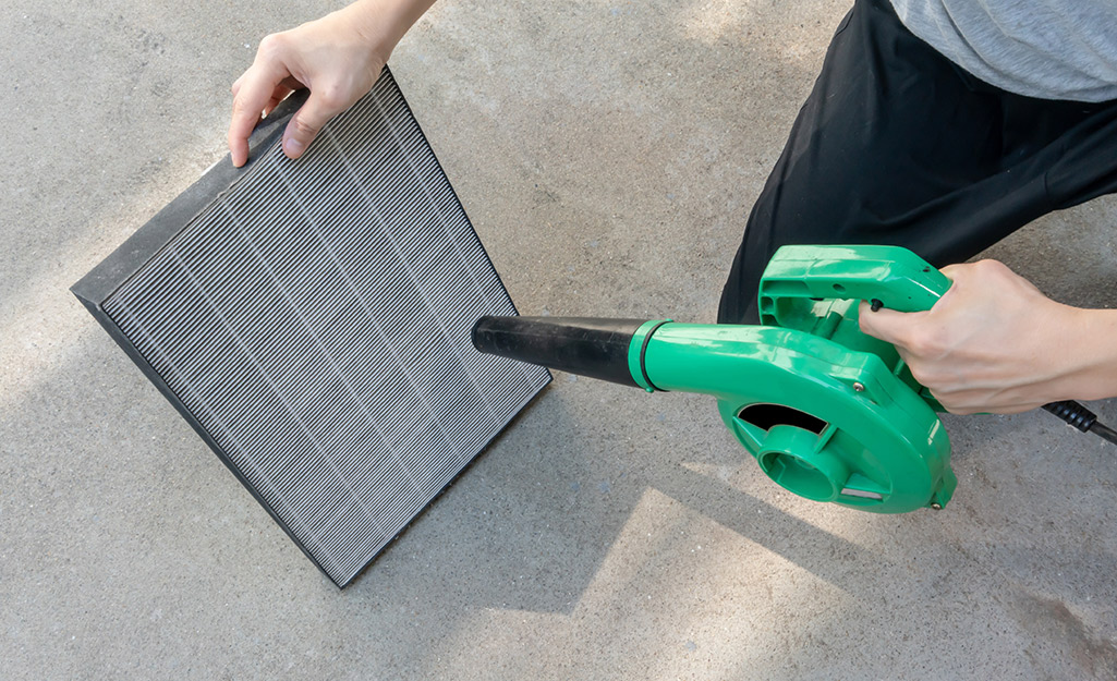 A person uses a handheld vacuum to clean an air filter.