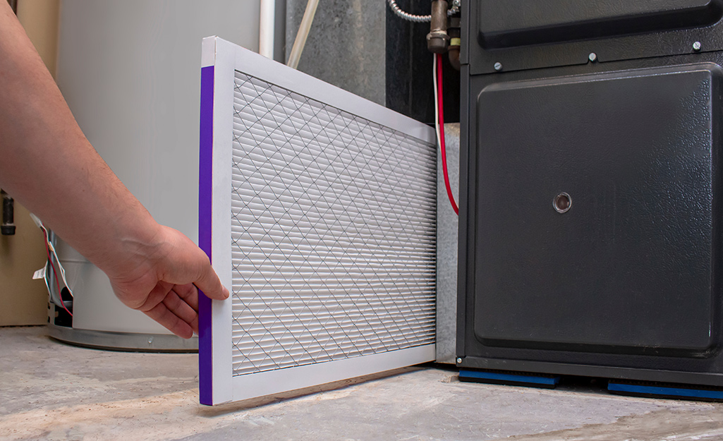 A person removes an air conditioner filter from an AC unit.