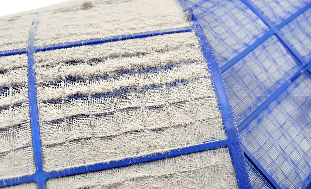 A dust-covered air conditioner filter lays next to a clean filter.