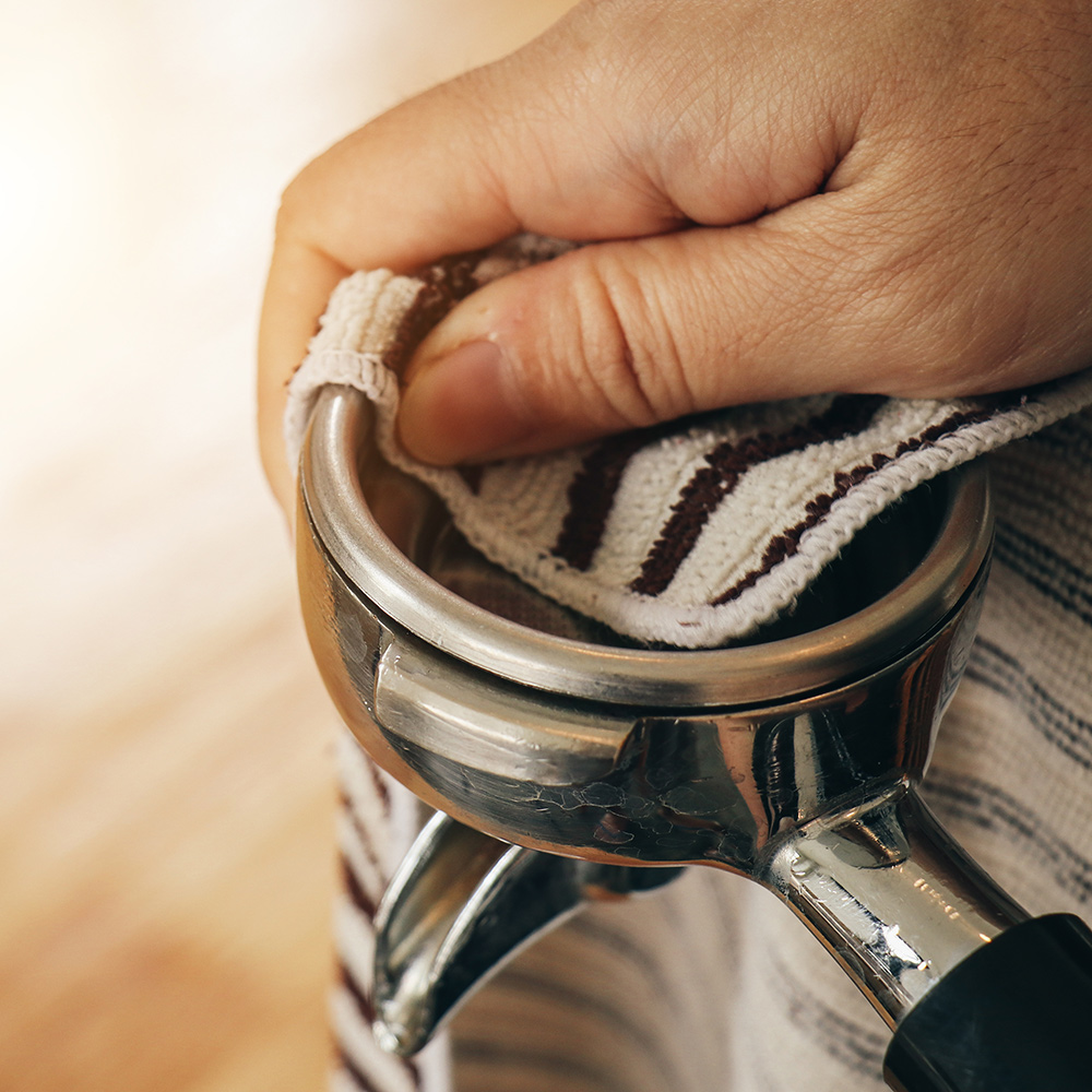 A person wipes the portafilter of an espresso machine with a cloth.