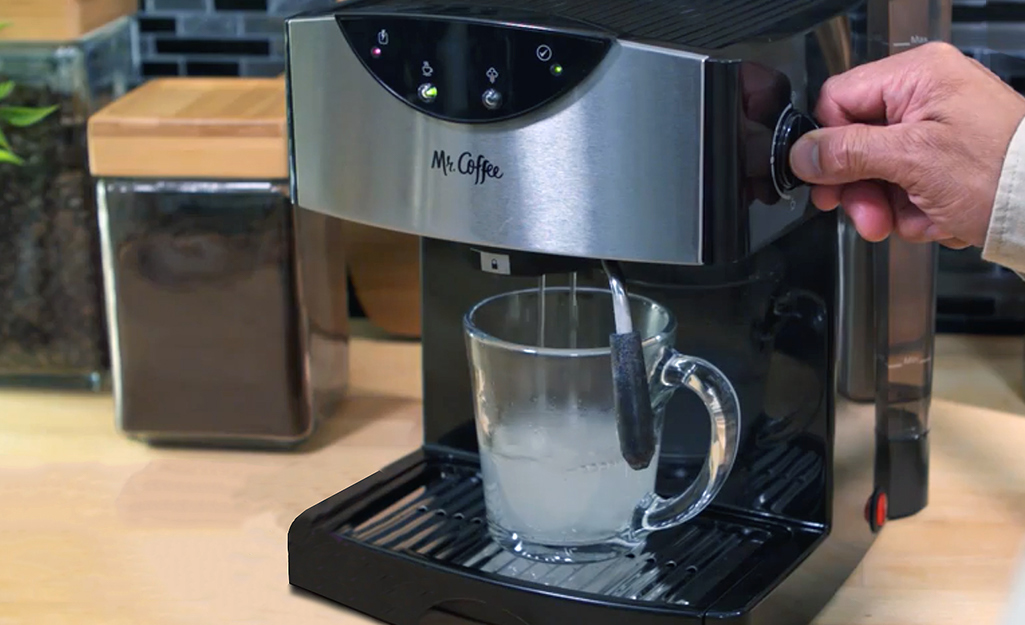A person flushes cleaning solution through the steam wand of an espresso machine,