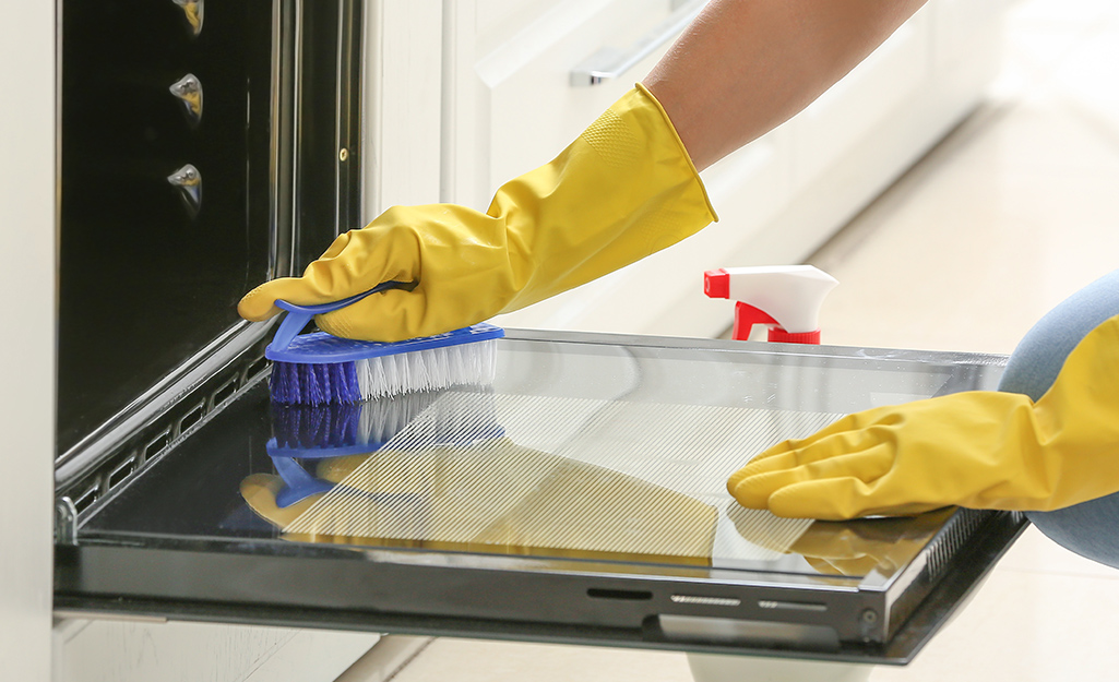 Someone cleaning inside oven door with a scrub brush.