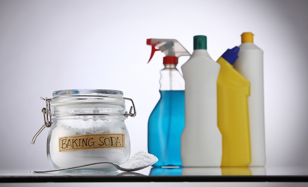 A glass jar of baking soda sitting next to other cleaning supplies.