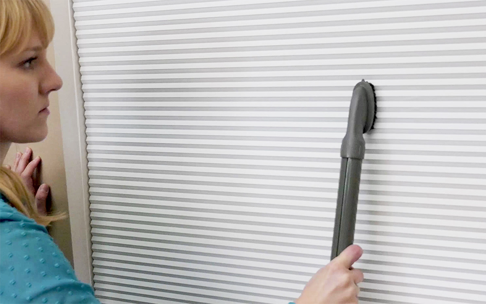 A person vacuuming blinds with a wand attachment