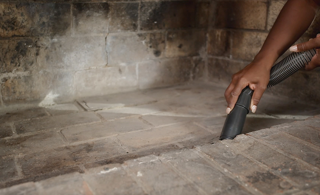 A person uses a vacuum hose to clean dirt from a fireplace.