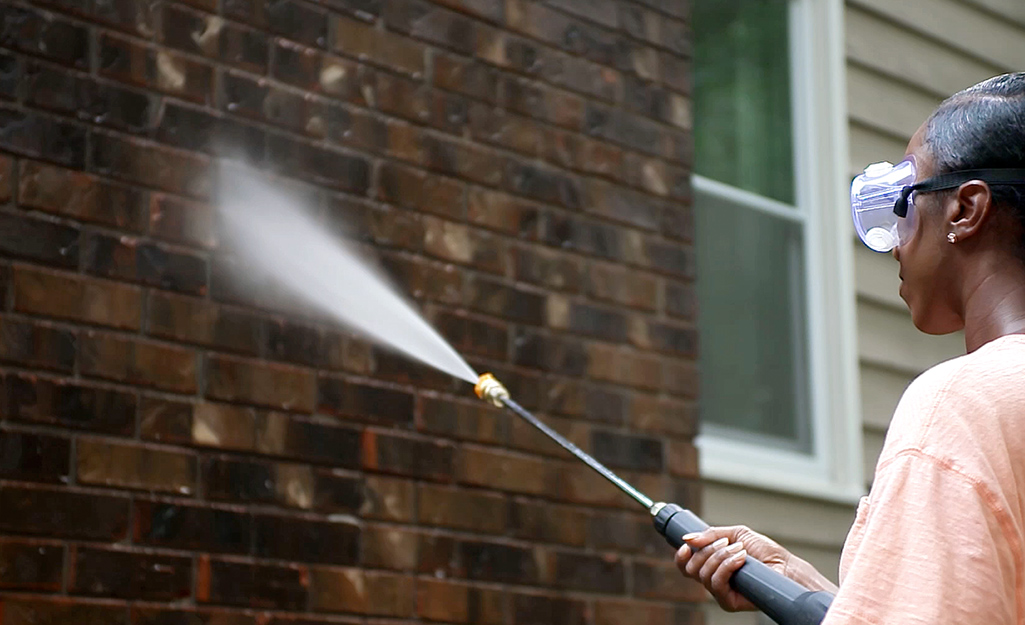 A person sprays the exterior brick wall of a house.