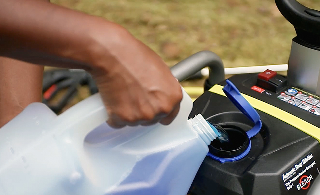 A person adds exterior washing detergent solution to a power washer tank.