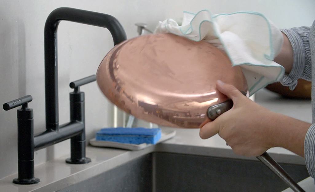 A person wipes down copper cookware.