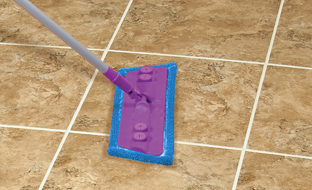 Someone using a mop to clean grout on a filed floor.