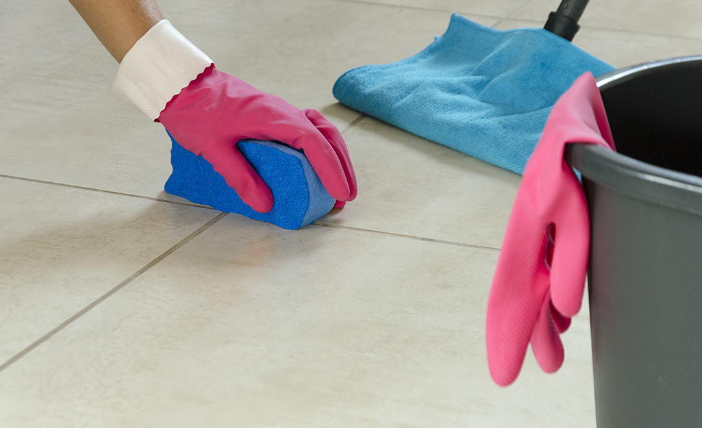 Someone cleaning grout on a tiled floor with a sponge.