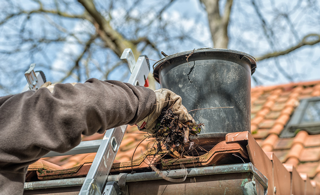 A person removing leaves from a gutter.