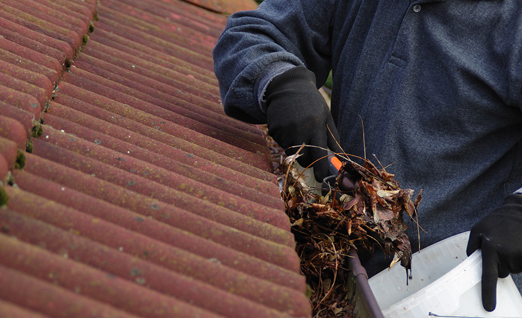 A person scooping gutter debris into a bucket.