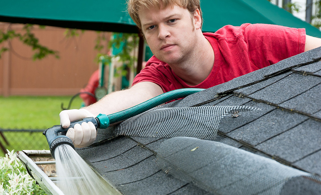 A person flushing a gutter with water from a garden hose.