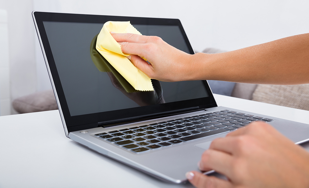 A person wiping a laptop screen with a microfiber cloth.