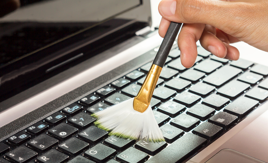 A person using a small brush to clean the keys of a laptop keyboard.
